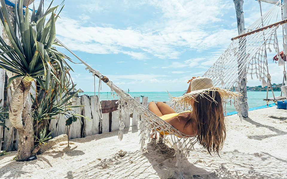 Frühbucher Urlaub: Frau liegt in Hängematte am Strand mit Meerblick